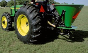 Closeup of a broadcast spreader attached to a John Deere tractor in a grassy field